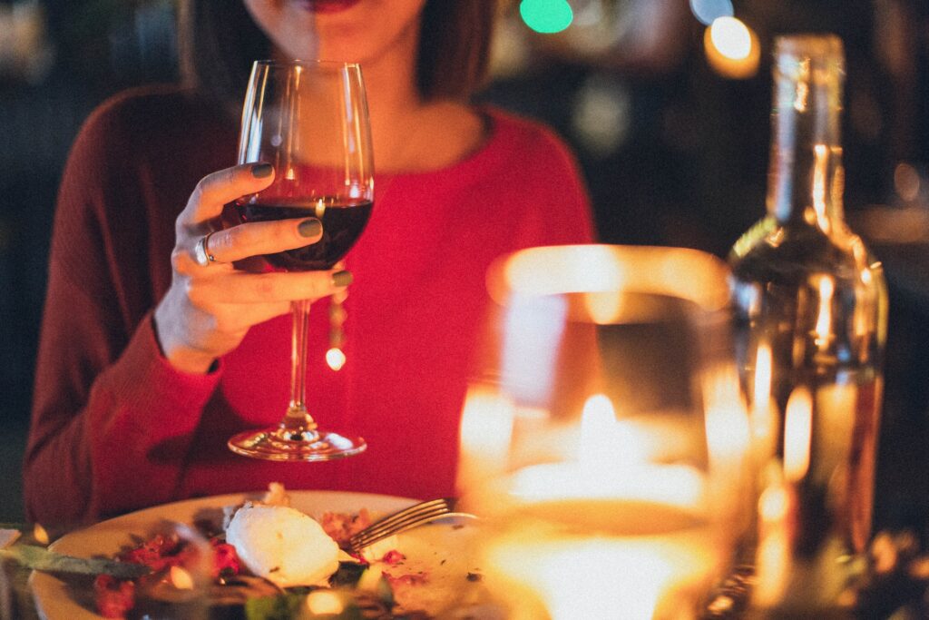 Closeup of woman drinking wine on a dinner date, showing how to impress her in person at dinner