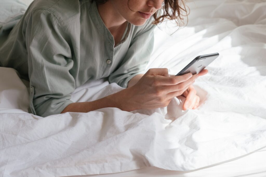 Woman using phone in bed, symbolizing how connecting over social media can be done anywhere