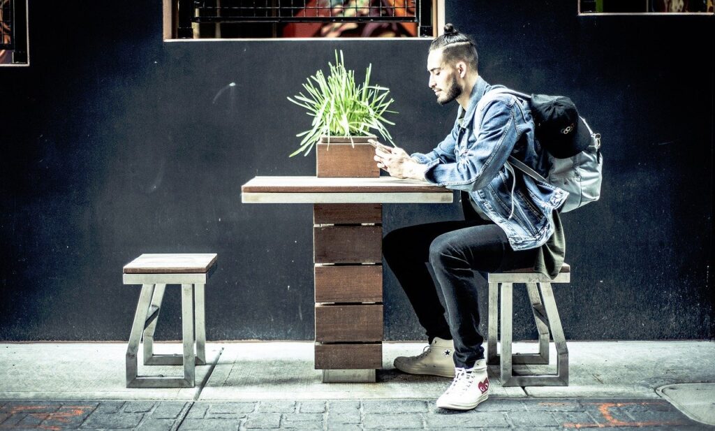 Man sitting at a table looking at his phone, illustrating effective dating profile creation